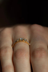 Ring TIDE | Trilogy in Gelbgold am Finger, Nahaufnahme – drei Brillanten in Krappenfassung mit funkelndem Diamantbesatz auf der Ringschiene