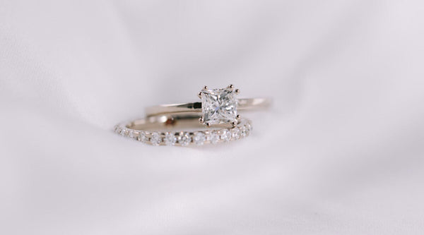 Princess-Verlobungsring aus 750er Weißgold mit 0,8 Karat Diamant in doppelter Krappenfassung, kombiniert mit Memoire-Ring von JUVELAN.