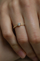 Ring AURA Rund in Gelbgold am Finger, Nahaufnahme von oben – runder Brillant in Sechs-Krappen-Fassung mit feinen Diamanten auf beiden Seiten der Ringschiene